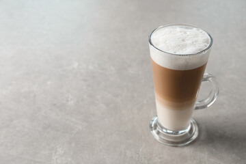 Glass cup of delicious layered coffee on light grey table, space for text