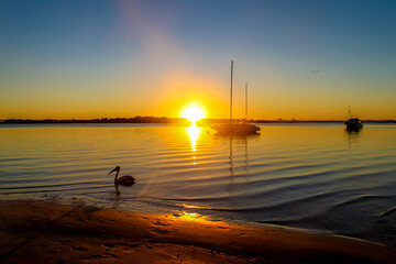 Boats anchored in Bribie Island Australia bay at sunset as sun disappears over the horizon with...