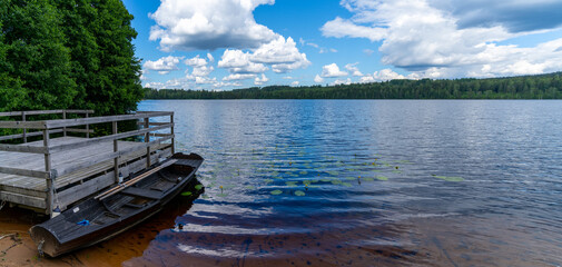 calm blue lake in the middle of the forest with a wooden dock and rowboat in the foreground