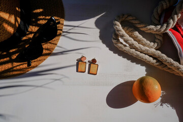 Beach bag, sunglasses, straw hat, earrings, orange fruit in palm leaves shadow on white background. Summer flat lay. Vacation concept. Copy space