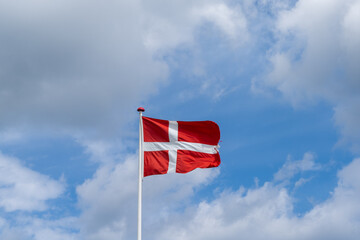 Danish flag flying in the wind under a blue sky with white cumuls clouds