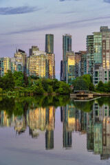 Fototapeta na wymiar View of Lost Lagoon in famous Stanley Park in a modern city with buildings skyline in background. Colorful Sunset Sky. Downtown Vancouver, British Columbia, Canada.