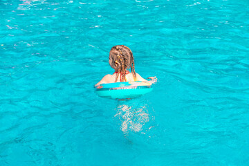 happy little girl playing with an inflatable ring in an outdoor pool on a hot summer day. family vacation at the resort