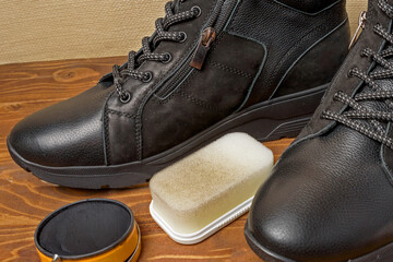 A jar of shoe polish and a sponge for shoe care near men's shoes on a wooden background close-up