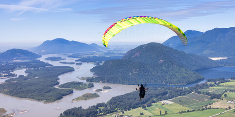 Adventurous Woman Flying on a paraglider around the Canadian Mountain Landscape. Harrison Mills...