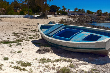 Fototapeta premium View of an old, wooden boat on the white sand of the Mediterranean coast. Rest at the sea. Djerba Island, Tunisia
