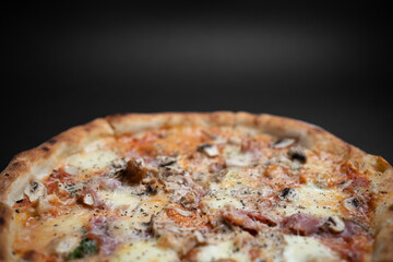 closeup of italian pizza with ham, mushrooms and cheese on black background