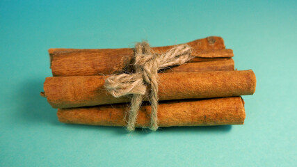 many sticks of cinnamon bark tied by a thread lie on a turquoise background side view. aromatic spice