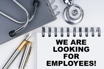 On the table are a stethoscope, a pen and a notebook with the inscription - WE ARE LOOKING FOR EMPLOYEES