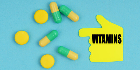 On a blue background, there are pills and a hand-sticker with the inscription - Vitamins
