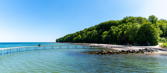 panorama of people at the Bay of Aarhus with the Infinite Bridge in the foreground and forest behind under a blue cloudless sky - Powered by Adobe