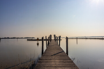 Fototapeta na wymiar Straight wooden bridge between calm waters towards the recreation area in the Atoll at Woldstrand Zeewolde beach, sunset on a spring day in Flevoland, Netherlands