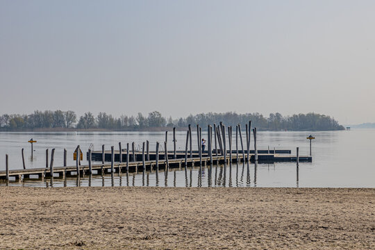 Wooden platform among calm waters with mature woman filming with her mobile phone, enjoying a sunny and relaxed day at Woldstrand Zeewolde beach recreation area, spring day in Flevoland, Netherlands