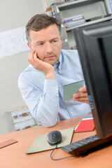 Fototapeta premium Man reading card and computer screen