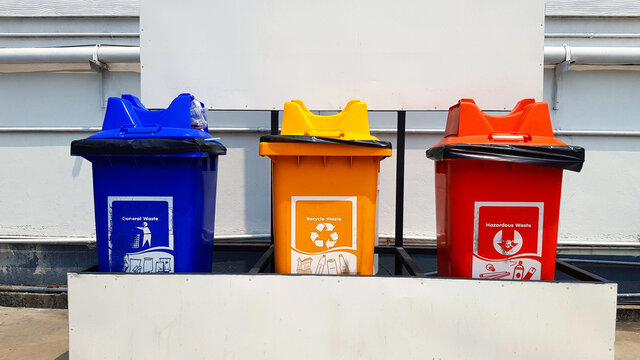 Blue, yellow and red bins for separate trash for reuse and disposal at park. Colorful trashcan for dumping used stuff or material with white gas or oil pipeline and panel background .