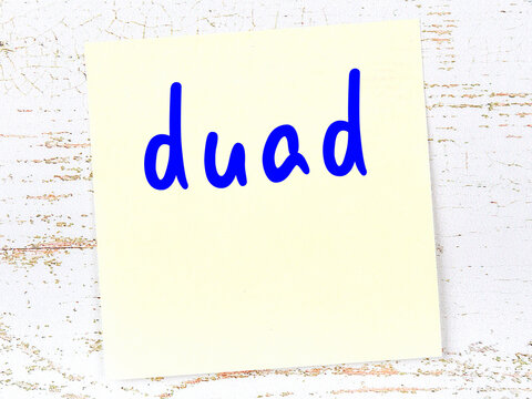 Yellow sticky note on wooden wall with handwritten word duad