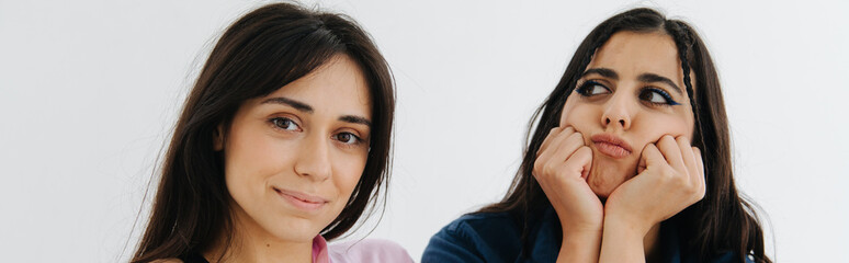 smiling armenian woman looking at camera near offended friend isolated on white, banner