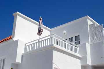 Modern White Apartment Building with Terrace & Furled Umbrella against Blue Sky
