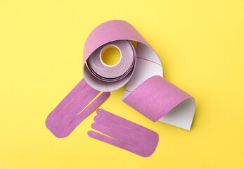 Bright kinesio tape roll and pieces on yellow background, flat lay