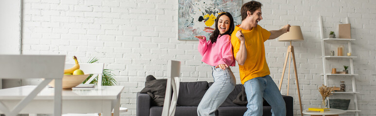 smiling young couple in casual clothes dancing in living room, banner