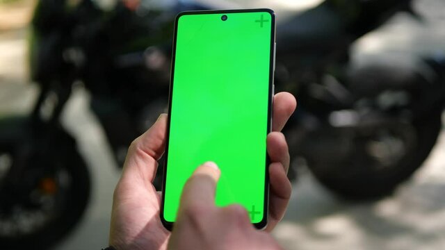 Biker hands using his cell phone with blank green screen chroma key with gestures and over shoulder static closeup view. Part of motorbike in the background.