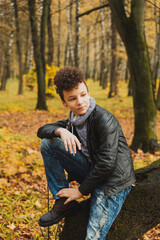 Curly brown-haired boy with a mohawk hairstyle in a leather jacket on an autumn background