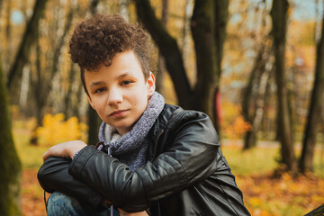 Curly brown-haired boy with a mohawk hairstyle in a leather jacket on an autumn background