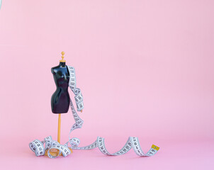A scaled-down mannequin on a pink background with a measuring tape