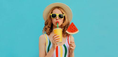 Summer colorful portrait of beautiful young woman drinking juice with lollipop or ice cream shaped slice of watermelon wearing a straw hat on blue background
