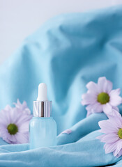 gentle blue background with a bottle of face cream, hands, with pink flowers, the concept of eternal youth, vertical photo