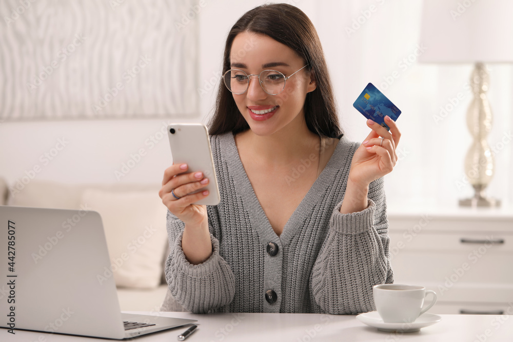 Wall mural woman with credit card using smartphone for online shopping at white table indoors