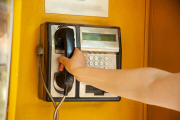 Woman using old and weathered oldstyle plublic pay phone in phone booth