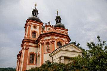 Fototapeta na wymiar Valec, Western Bohemia, Czech Republic, 19 June 2021: Baroque red and yellow church of the Holy Trinity with towers near castle at summer day