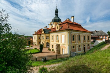 Nebilovy, Czech Republic - September 9 2018: View of the castle with yellow facade and red roof. Sandy path, green grass in front of the building. Sunny day with blue sky and clouds. - Powered by Adobe