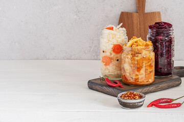 Healthy probiotic fermented food: kimchi cabbage and sauerkraut in glass jars on the dark kitchen board on a white wooden table. Great support the immune system. Concept healthy vegetarian food.