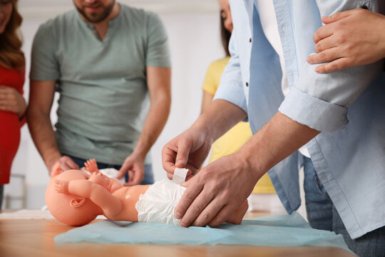 Future fathers and pregnant women learning how to swaddle baby at courses for expectant parents indoors, closeup