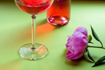 Romantic dinner or breakfast. Close up of creative summer composition with rose wine in a large glass and beautiful peonies on a green background.