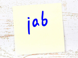 Yellow sticky note on wooden wall with handwritten word jab