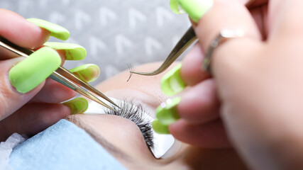 Obraz na płótnie Canvas a young model is lying on the procedure of eyelash extension the hands of the master are close up holding tweezers and pasting the eyelash