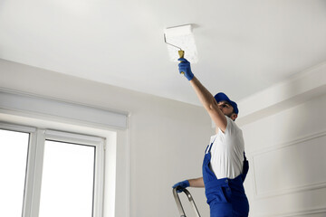 Handyman painting ceiling with white dye indoors, space for text