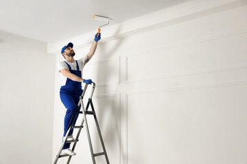 Handyman painting ceiling with white dye indoors, space for text