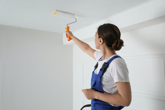 Worker painting ceiling with white dye indoors, back view. Space for text