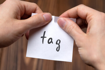 Hands of a man tearing a piece of paper with inscription tag