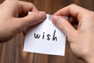 Hands of a man tearing a piece of paper with inscription wish