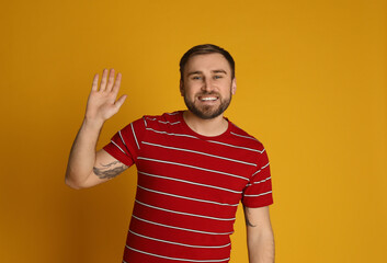 Happy young man waving to say hello on yellow background