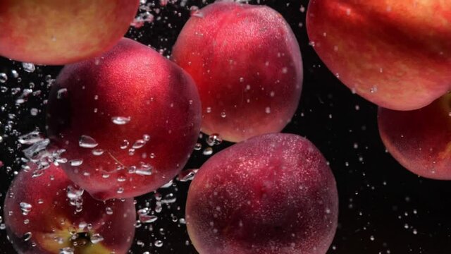 ripe red nectarines fall into water on black background