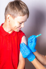 A nurse in a white cap, disposable mask and blue gloves injects the vaccine through a syringe into...
