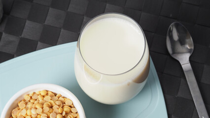 Soy milk with no sugar added in a glass on a green color plastic plate mat. Close-up images of home made healthy soy milk drink and soy beans in small bowl. Black background in a studio shot. Soymilk.