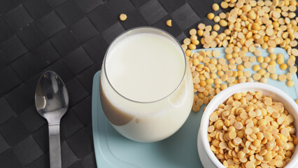 Soy milk with no sugar added in a glass on a green color plastic plate mat. Close-up images of home made healthy soy milk drink and soy beans in small bowl. Black background in a studio shot. Soymilk.
