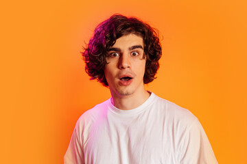 Amazed man looking at camera isolated on orange with purple lighting